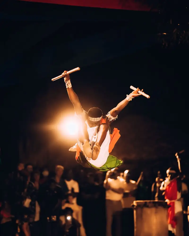 Un danseur en plein saut, bâtons levés, au-dessus du public de l'IZUBAFEST 2026