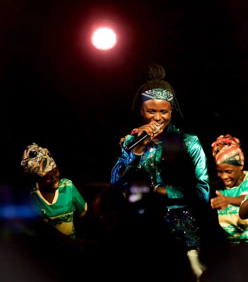Une chanteuse en tenue verte chante au micro, entourée de danseuses