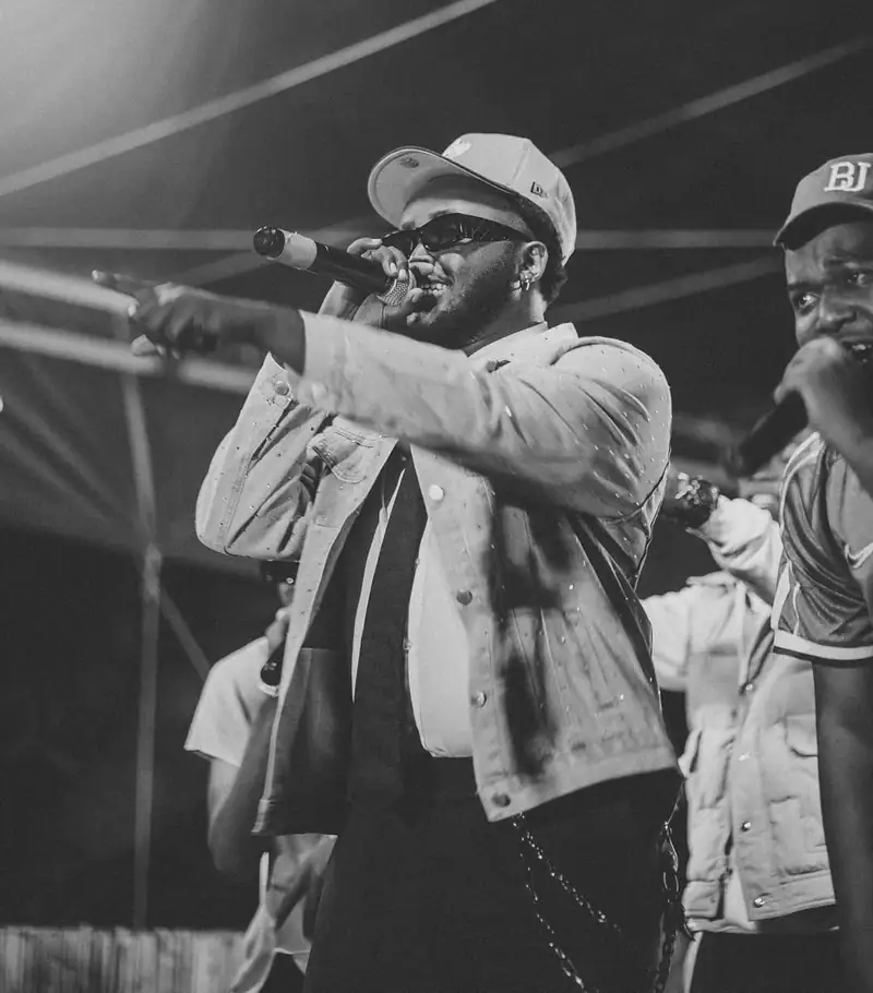 Un rappeur en casquette blanche chante au micro, en noir et blanc